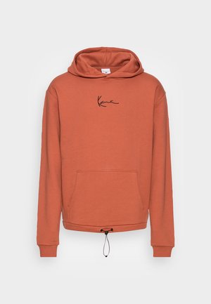 Sweat-shirt à capuche orange rouille avec poche avant, ourlet à cordon noir, et petit logo manuscrit noir centré sur la poitrine.