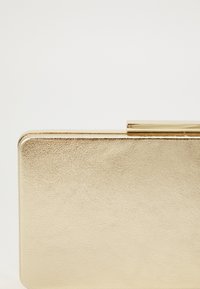 Gylden metallisk clutche med en glatt lærtekstur, rektangulær form og en elegant lås. Polert finish med minimal detaljering.