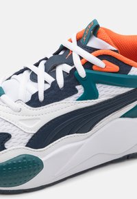 PUMA sportcipők fehér hálós anyagból, tengerészkék és teal kiegészítőkkel, narancssárga textile belsővel és jellegzetes fűzési rendszerrel, amely texturált talpra épül.
