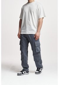 Bílá bavlněná trička s volným střihem, spojená se šedými cargo kalhotami s několika kapsami. Celkový vzhled doplňují černobílé tenisky.