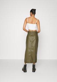 Jupe midi en similicuir vert olive avec une coupe ajustée et une fente au dos, associée à un crop top blanc et des bottines noires.