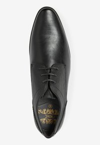 Zapato de vestir negro con un upper de cuero suave y paneles de tela texturizada, con cinco ojetes para los cordones y un diseño de puntera puntiaguda.