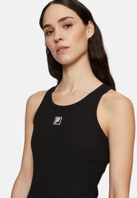 Débardeur noir côtelé avec un col rond et un détail de logo blanc sur la poitrine. Fait en tissu extensible, design ajusté.