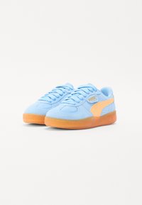 Light blue suede sneakers with orange accents, featuring round laces, a padded collar, and a translucent rubber sole. Logo displayed on side.