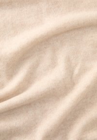 Beige strikstof med en blød tekstur, der har et subtilt meleret mønster og bløde folder, som skaber et glat udseende.