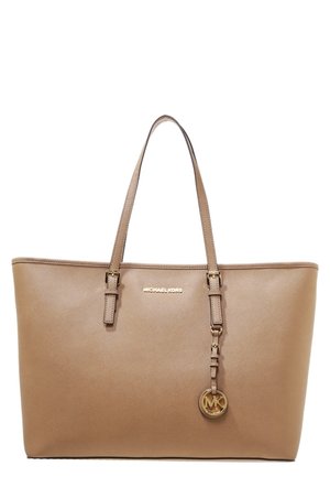 Beżowa torba typu tote Michael Kors z podwójnymi paskami na ramię oraz złotym brelokiem z logo zawieszonym na prawym pasku.