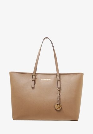 Beżowa torba typu tote Michael Kors z podwójnymi paskami na ramię oraz złotym brelokiem z logo zawieszonym na prawym pasku.