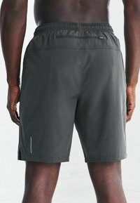 Szare szorty sportowe z elastycznym paskiem w talii, bocznymi kieszeniami i zapinaną na zamek kieszenią z tyłu; cechują się starannym wykończeniem i bocznymi rozcięciami dla lepszej swobody ruchów.