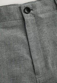 Graues Fischgrätgewebe mit diagonalen Streifen, ausgestattet mit einem schwarzen Knopfverschluss an der Taille und einem klaren, taillierten Design.