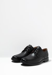 Scarpe di pelle nera con finitura liscia, punta arrotondata e design con lacci. Accenti laterali leggermente testurizzati e suola bassa in gomma.