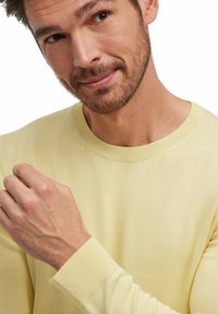 Maglione leggero giallo con scollo a giro e polsini a costine, caratterizzato da una superficie liscia e un design aderente. Stile minimalista.