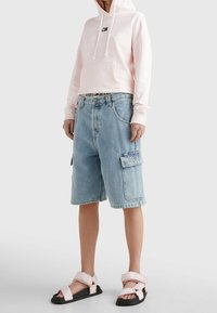 Světle růžová zkrácená mikina s přední kapsou. Modré denimové cargo šortky s bočními kapsami. Černé ploché sandály s růžovými popruhy.