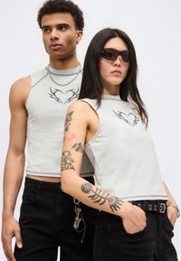 Δύο μοντέλα φοράνε ταιριαστά αμάνικα τοπ με σχέδια καρδιών· το ένα έχει γυαλιά ηλίου και τατουάζ, και τα δύο φοράνε μαύρο παντελόνι με αξεσουάρ.