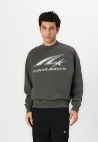 Gray sweatshirt with ribbed neckline and cuffs, featuring a prominent silver logo design on the front. Soft fabric, relaxed fit.