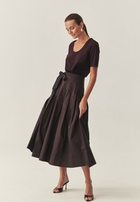 Bordowy top z krótkim rękawem w połączeniu z czarną spódnicą w kształcie dzwonu o wysokim stanie, z plisami i paskiem do zawiązania w talii. Uzupełnione otwartymi szpilkami.