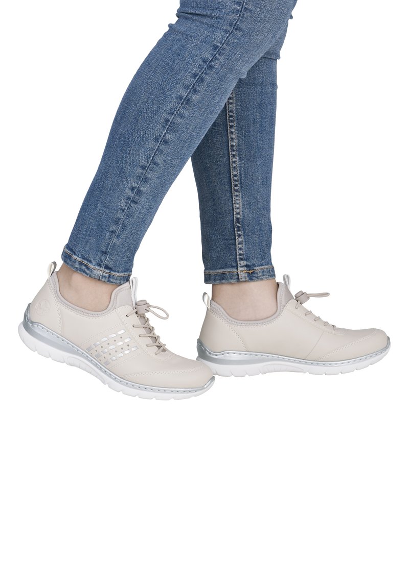 Baskets beiges avec une tige en cuir lisse, un design à lacets et des accents texturés. Semelle légère avec une bordure argentée autour de la base.