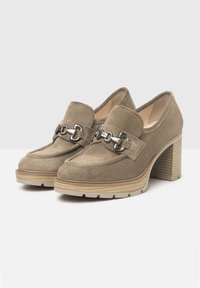 Mocasines de tacón alto de ante beige con un destacado detalle de cadena plateada en la parte superior, que cuentan con una plataforma texturizada y un tacón a rayas.