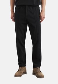 Black elastic-waist pants with vertical seams and a relaxed fit. Tapered leg design complements brown suede lace-up boots.