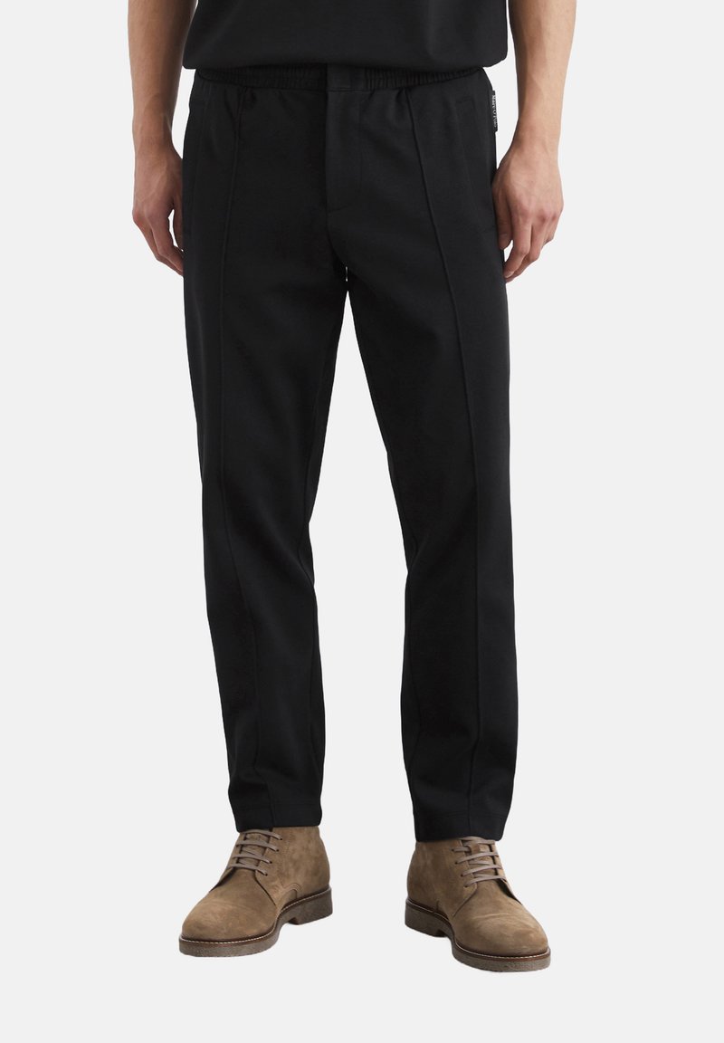Black elastic-waist pants with vertical seams and a relaxed fit. Tapered leg design complements brown suede lace-up boots.