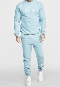 Světlemodrý svetr s kulatým výstřihem, s bílým textem. V kombinaci s odpovídajícími tepláky se zúženým střihem a bílými akcenty.