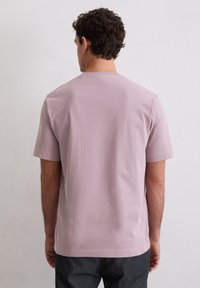 Rövid ujjú, kerek nyakú póló világos mályva pamutból, sima textúrával; laza szabás, látható minták vagy díszítések nélkül.