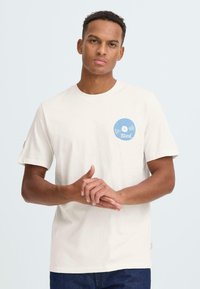 Roomkleurig katoenen T-shirt met korte mouwen, voorzien van een blauwe vinylplaatgrafiek op de linkerborst en een label op de mouw.