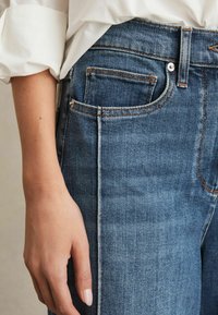 Jeans in denim blu scuro con una vestibilità strutturata, dotati di tasche tradizionali, cuciture visibili e una leggera texture lavata.