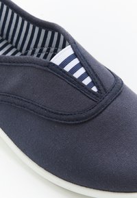 Scarpa slip-on in tela blu marina con cuciture di accento bianche, tomaia testurizzata e fodera in tessuto a righe. Punta arrotondata e suola flessibile.