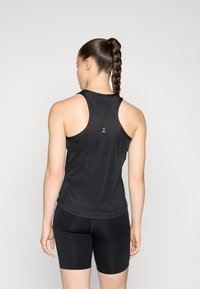Černý sportovní top s síťovanou texturou a designem na zádech, spárovaný s černými cyklistickými šortkami. Na zadní straně má minimální branding.