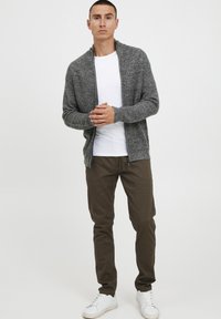 Grå strikket cardigan med lynlås i front, struktureret stof, båret over en hvid T-shirt. Kombineret med olivengrønne bukser og hvide sneakers.