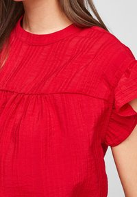 Blusa rossa con texture, maniche corte a volant e vita arricciata, dotata di un collo a giro morbido e un discreto motivo a righe.