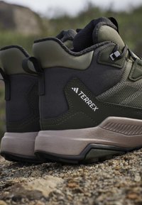 Close-up of two green and beige Adidas Terrex hiking boots resting on rocky ground outdoors.