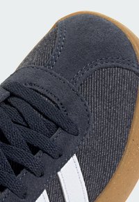 Dark grey sneaker featuring a suede and striped textile upper, white stripes, and a rubber gum sole. Laces are black and woven.