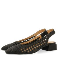 Zapatos de slingback negros tejidos con punteras puntiagudas, lados abiertos y un pequeño tacón cuadrado. Presentan un interior de cuero marrón claro para crear contraste.