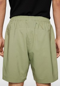 Vihreät shortsit, joissa on joustava vyötärö, teksturoitu yläpaneeli ja sileä alaosa. Ominaisuuksiin kuuluu vapaa istuvuus ja reiden puoliväliin ulottuva pituus.