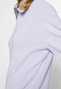 Pullover a maglia di un delicato viola chiaro con una mezza zip e una texture a coste. Presenta un colletto piccolo. Il design è a vestibilità rilassata con un orlo curvo.
