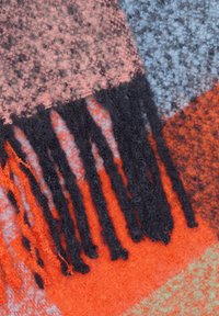 Wollen deken met geometrische patronen in oranje, roze, blauw en grijs, voorzien van lange zwarte franjes langs de randen, die textuur en detail toevoegen.
