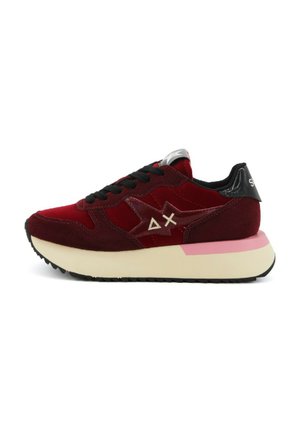 Sneaker in suede rosso con suola bianca e rosa, lacci neri e dettagli lucidi. Presenta un logo sul lato e un tallone imbottito.