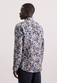 Camicia stampata floreale con fiori multicolori in blu, bianco e marrone su uno sfondo scuro. Maniche lunghe, polsini con bottone, orlo curvo.