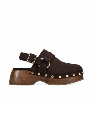 Zueco marrón oscuro con suela de plataforma de madera, tachuelas doradas a lo largo del borde de la suela y correa ajustable para el tobillo con hebilla dorada.