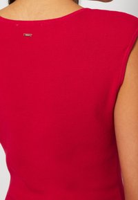 Top sans manches côtelé rouge avec un col rond et une petite étiquette au dos, mettant en valeur une texture lisse et un design ajusté.