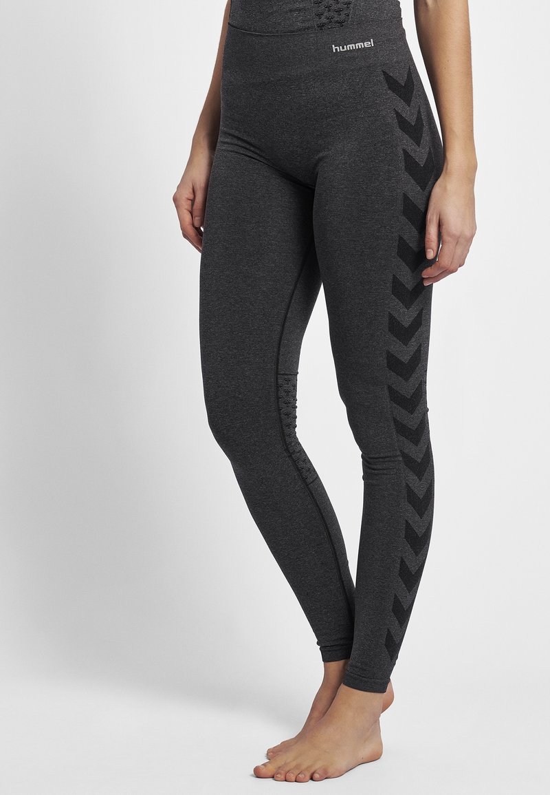 Leggings sportivi grigi con vita alta. Presentano motivi a chevron neri sui lati e dettagli testurizzati vicino alle caviglie.