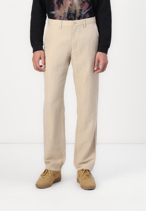 Pantaloni di lino beige con vestibilità dritta. Presentano una chiusura con bottone frontale e passanti per la cintura. Abbinati a sneakers color cammello per un look casual.