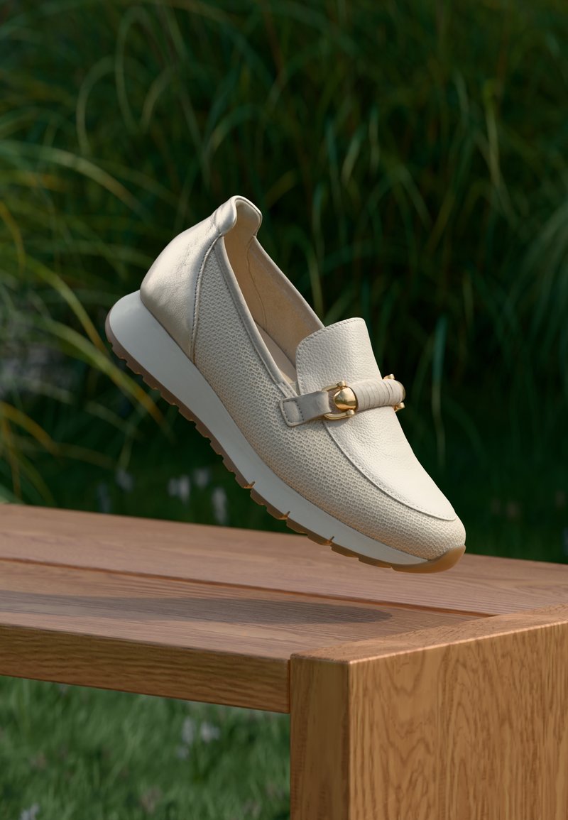 Μπεζ δερμάτινα μοκασίνια με υφή στην επιφάνεια και χρυσή λεπτομέρεια, τοποθετημένα σε ένα ξύλινο παγκάκι, με παχιά λευκή σόλα και ανυψωμένη πίσω πλευρά.