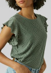 Haut vert à manches courtes en tissu ajouré, avec des manches à volants et des motifs en losange. Matière légère avec des détails texturés.