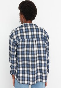 Modrá a bílá kostkovaná flanelová košile s dlouhými rukávy, zadním dílem s klopou a zapínáním na knoflíky na manžetách. Měkká textura, volný střih.