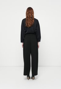 Schwarzes Langarmoberteil mit lockerer Passform, kombiniert mit hochtaillierten schwarzen Hosen. Glatter Stoff und weites Bein-Design, ergänzt durch hohe Absätze.