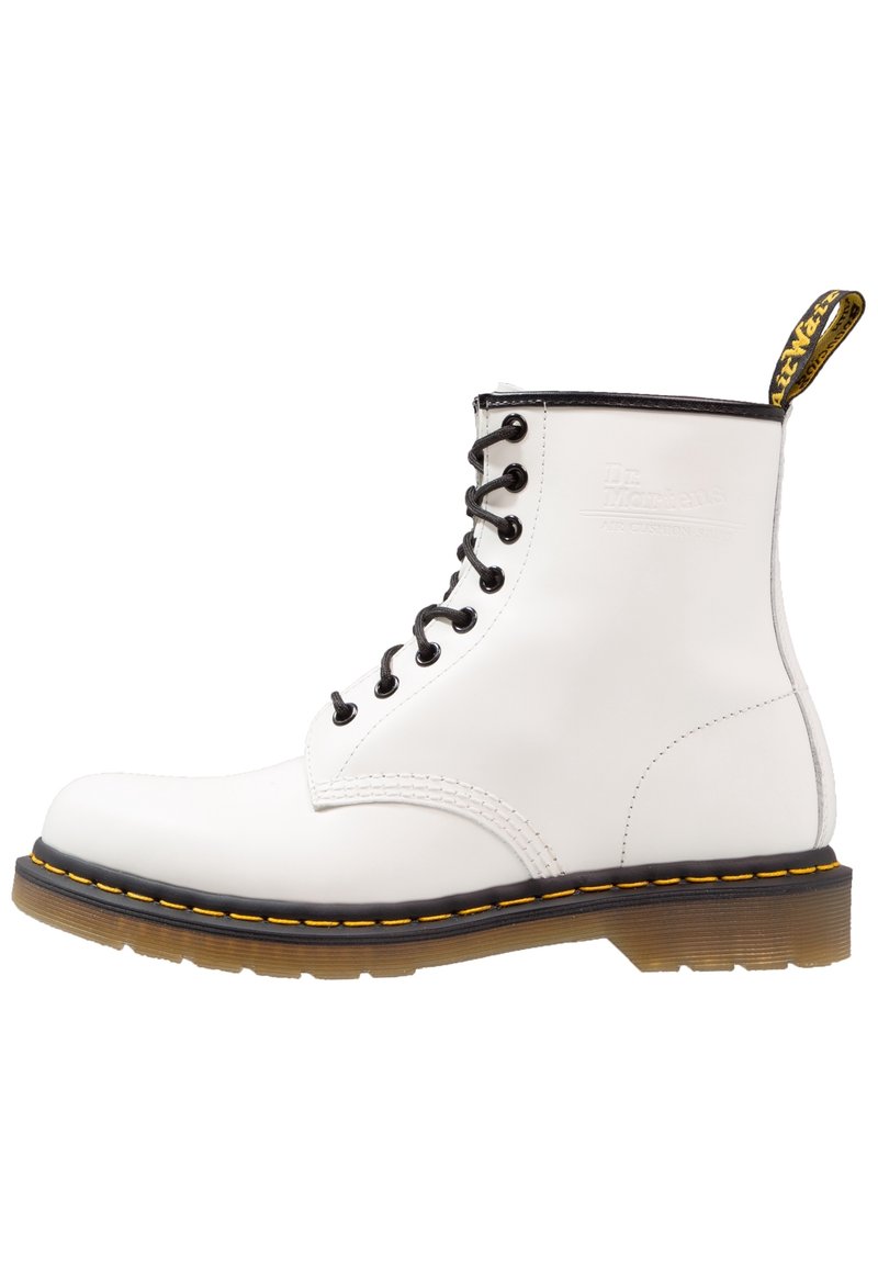 Botte en cuir blanc à lacets avec œillets noirs, coutures jaunes, semelle marron et languette de tirage brandée à l'arrière.