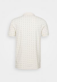 Polo shirt crema con maniche corte, caratterizzata da un motivo a piccoli rombi ripetuti in marrone scuro e un colletto a contrasto.