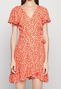 Červené květinové zavinovací šaty s krátkými volánkovými rukávy, výstřihem do V a rozšířenou sukní s třepeným lemem. Lehký materiál s malými bílými květinami.